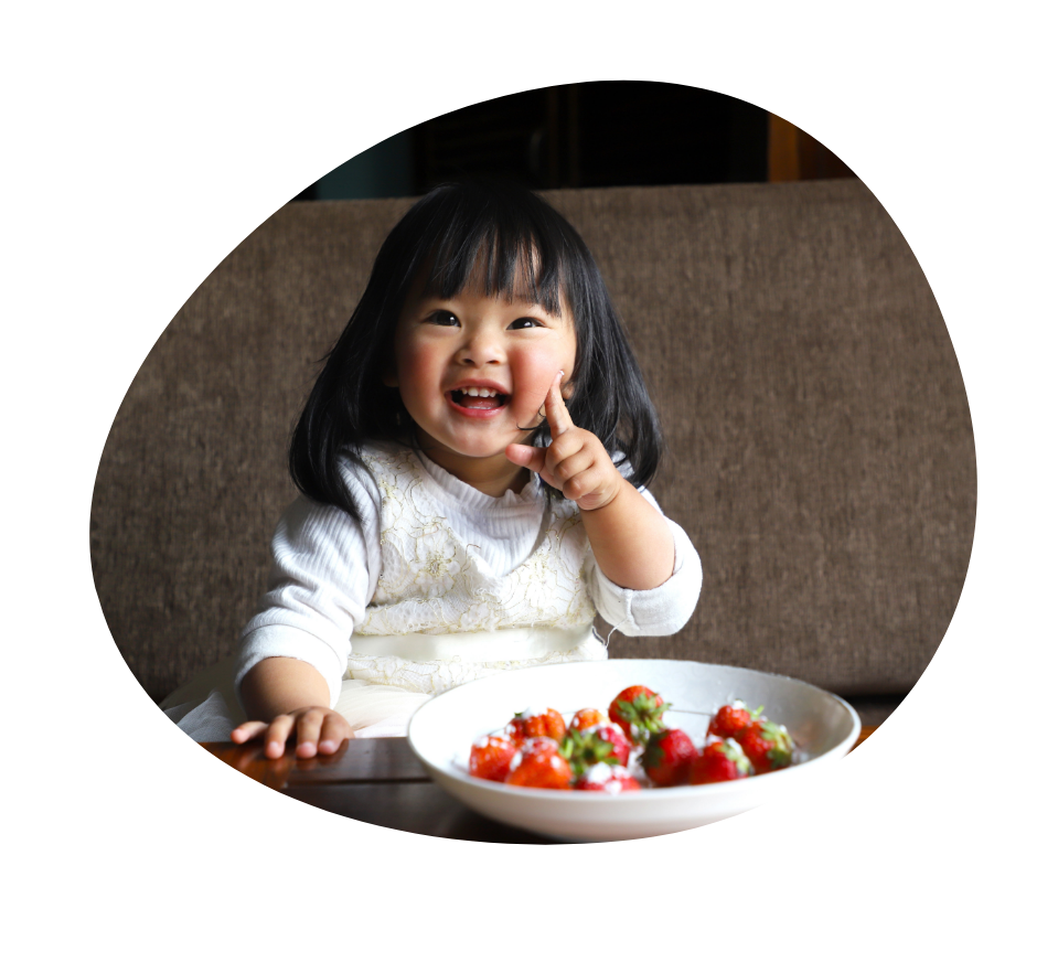 smiling toddler with a plate of strawberries in front of her strawberries